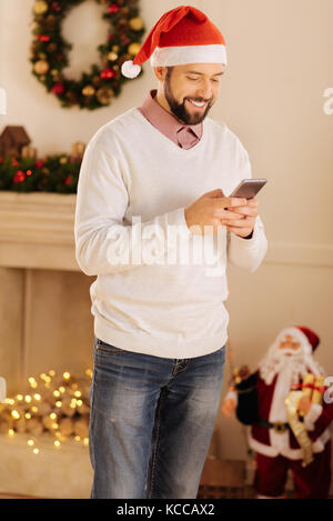 Freudiger Mann in Santa Hut Lesen von SMS-Nachrichten Stockfoto