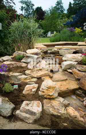 Das Errichten eines neuen Rock Garden nach dem Installieren einer handgefertigten Naturstein Wasserfall in einem Englischen Garten in Großbritannien Stockfoto