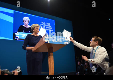 Der Komiker Simon Brodkin, auch bekannt als Lee Nelson, konfrontiert Premierministerin Theresa May während ihrer Keynote-Rede auf der Conservative Party Conference im Manchester Central Convention Complex in Manchester. Stockfoto