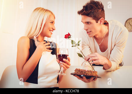 Ein junger stattlicher Mann mit einer Rose in der Hand gibt Geburtstagstorte überrascht mit seiner schönen Mädchen. Stockfoto