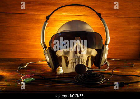 Schädel in Gläsern und mit Kopfhörern auf einem alten Holz- Hintergrund. Ein menschlicher Schädel von Kerzen auf Holzboden Leuchten, das Konzept von Halloween. Stockfoto