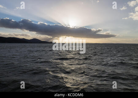 Leistungsstarke Sonnenstrahlen, die sich durch einige Wolken über einem See Stockfoto