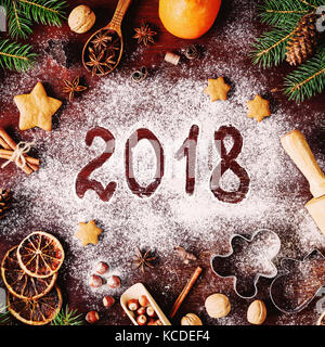Silvester oder Weihnachten 2018 auf Mehl geschrieben, Weihnachtsschmuck, Ausstechformen, Orangen, Gingerbread cookies, Gewürze, Nüsse und Tannenbaum um. SQ Stockfoto
