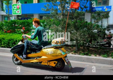 Modische junge Chinesen teenager Reiten auf scooter Motorrad in Qingdao China city centre Road street tragen Verschmutzung facemask Provinz Shanxi Stockfoto