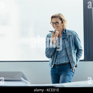 Weibliche Führungskräfte sprechen über Lautsprecher. Geschäftsfrau im Handy beim Stehen in Office. Stockfoto