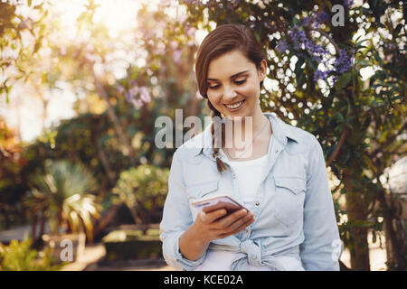 Schöne Frau mit Handy in einem Garten. Junge weibliche Plaudern auf Smart Phone im Freien. Stockfoto