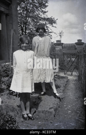 1920s, historische Bild zeigt eine junge Frau und kleines Mädchen stand außerhalb eines Hauses tragen die weiblichen Moden des Tages, England, UK. Stockfoto