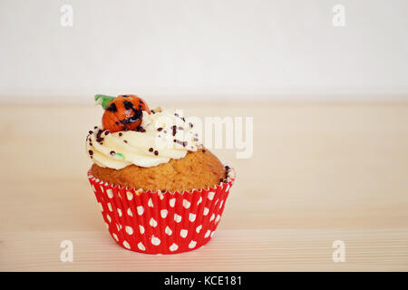 Cupcake dekoriert mit Sahne und Marzipan Kürbis an Halloween auf dem beigen Hintergrund Stockfoto