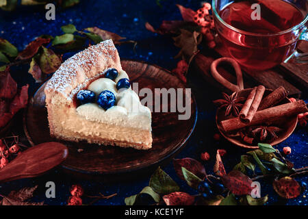 Hommemade Kruste Kuchen mit wipped Cream, Blaubeeren und Kürbispüree auf einem dunklen Hintergrund mit Blättern und Zimt. close-up ein Stück Kuchen. dunklen Essen Fotografie. Herbst noch Leben mit Gebäck. Stockfoto