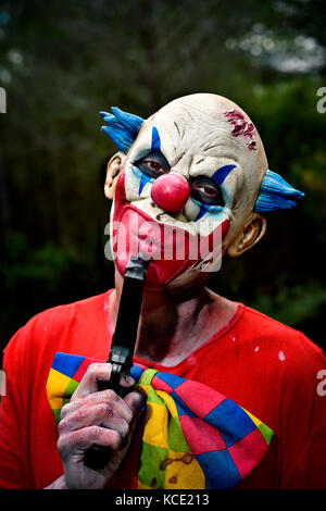 Nahaufnahme der Ein unheimlich bösen Clown in den Wäldern tragen eine schmutzige Kostüm bläst seine Waffe Stockfoto