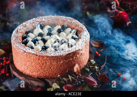 Sahne und Heidelbeerkuchen mit einem Shortbread Kruste auf einem dunklen Hintergrund gepeitscht. dunklen Essen Fotografie mit Rauch. Traditionelle Pumpkin Pie in einem Halloween Stillleben mit Gebäck. Stockfoto