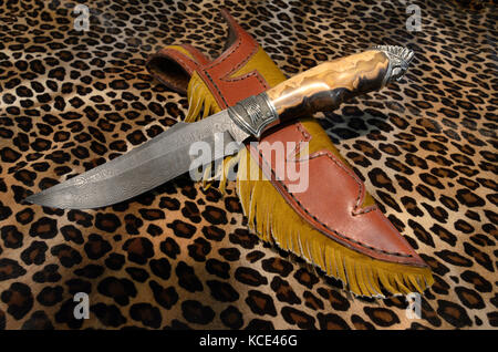 Ein feststehendes Messer Damast Messer und Scheide auf einem Leopard wie Haut Hintergrund angezeigt. Stockfoto