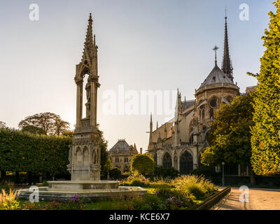 Rückansicht der Kathedrale Notre-Dame de Paris bei Sonnenuntergang mit dem Brunnen der Jungfrau im Vordergrund. Stockfoto