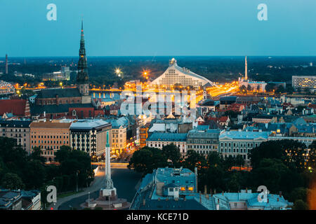 Riga, Lettland - 2. Juli 2016: Luftaufnahme von stadtbild in Abend Nacht Leuchten aufleuchten. Sommer Blick von oben auf die St. Peter Kirche, Freiheitsdenkmal ein Stockfoto