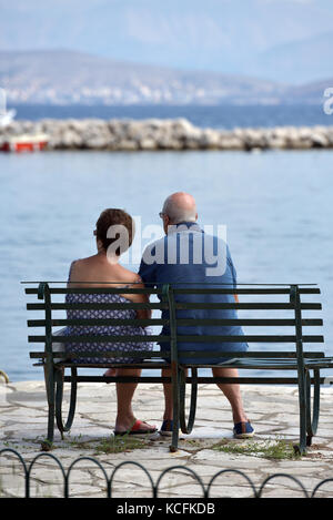 Ein älteres Paar oder ein Paar auf einer Bank sitzen, Blick auf das Meer, die Berge und das Meer im Hintergrund in Griechenland. Stockfoto