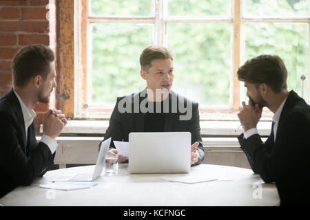 Junge schwere Boss vor laptop Consulting zwei männliche Mitarbeiter während des Briefings treffen. leitenden Angestellten sprechen über Unternehmensziele zu coworke Stockfoto