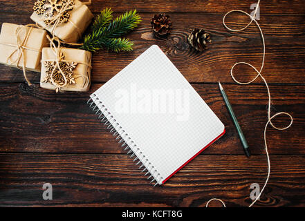 Weihnachten Zusammensetzung der Geschenk Kraftpapier Boxen und Holzspielzeug, Mais und Hinweis mit Stift auf hölzernen Hintergrund Stockfoto