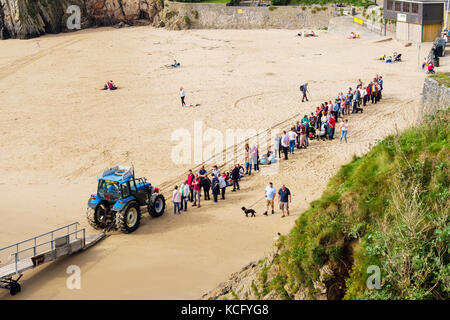 Lange Schlange von Menschen durch Jetty Traktor auf Schloss Strand für Bootsfahrt zur Insel Caldey. Tenby, Pembrokeshire, Wales, Großbritannien, Großbritannien Stockfoto
