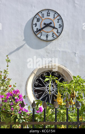 Eine dekorative Uhr auf einer weißen Turm über ein kreisförmiges Glasfenster auf eine Kirche in der griechischen Stadt kassiopi auf der Insel Korfu. Stockfoto