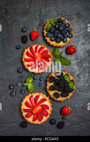 Torten mit Zitronencreme und frische Beeren auf schwarzem Hintergrund, Ansicht von oben Stockfoto