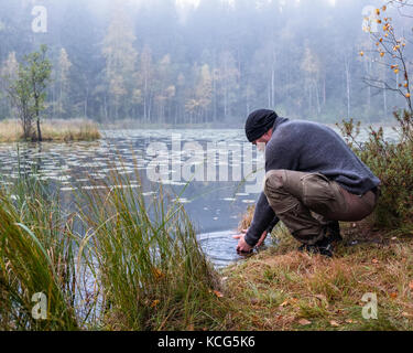 Wanderer waschen sein Angesicht zu Herbst morgen im Nationalpark, Finnland Stockfoto