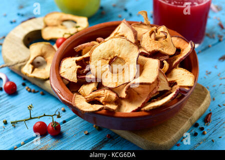 Nahaufnahme von einigen Schichten von getrockneten Apfel diente als Vorspeise oder Snack, auf einem blauen rustikalen Holztisch, neben einem Glas mit einem roten Smoothie Stockfoto