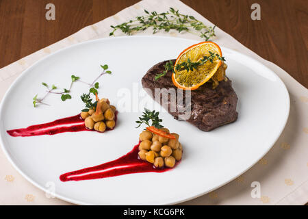 Saftiges Rindersteak mit orange Sauce mit grünen und Kichererbsen Stockfoto