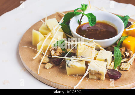 Verschiedene Arten von Käse mit Honig, Nüssen und Früchten auf runden Holzbrett Stockfoto