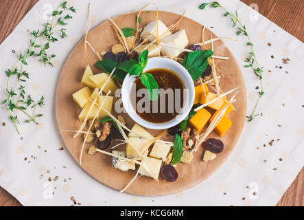 Verschiedene Käsesorten mit Honig, Nüssen und Früchten auf rundem Holzbrett Stockfoto