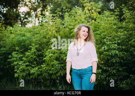 Junge schöne ziemlich Plus size kaukasische Mädchen Frau in weißer Bluse und Jeans das Leben genießen und lächelnd stehen auf Sommer grünen Wald angezogen Stockfoto