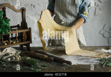 Junge Frau in Schürze Holding ein Teig für hausgemachte Nudeln im rustikalen Küche Stockfoto