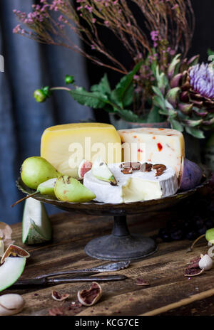 Der verschiedene Käse, frisches Obst und Gartenblumen auf altem Holzhintergrund Stockfoto