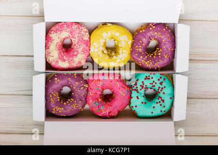 Bunte Donuts im Karton auf dem weißen Holz- Hintergrund Stockfoto