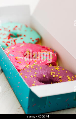 Bunte Donuts im Karton auf dem weißen Holz- Hintergrund Stockfoto