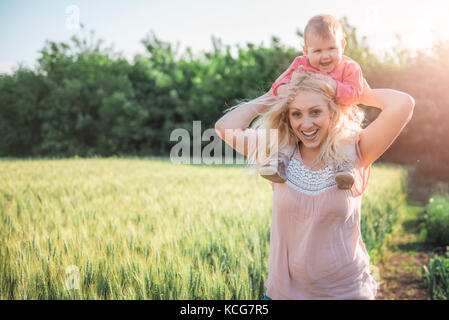 Mutter mit Baby Tochter Huckepack und stehen durch das Weizenfeld Stockfoto
