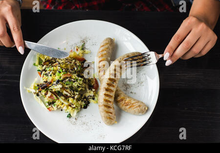 Junge Frau essen bayerische Würstchen mit Salat von frischem Gemüse Stockfoto