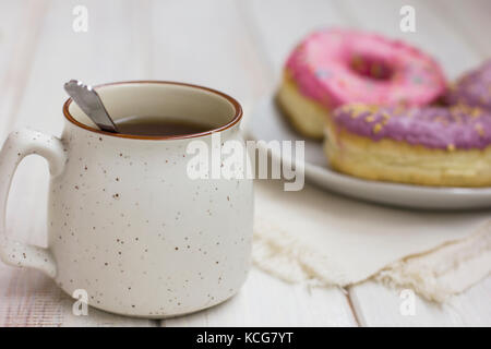 Die Tasse Tee und frische Donuts im weißen Platten auf hölzernen Hintergrund Stockfoto