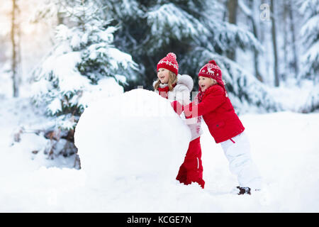 Kinder bauen Schneemann. Kinder bauen Schneemann spielen im Freien an sonnigen verschneiten Wintertag. outdoor Spaß für die ganze Familie auf Weihnachten Urlaub. Junge und Mädchen spielen Stockfoto