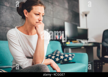 Traurige Frau sitzt auf einem Sofa im Wohnzimmer Stockfoto