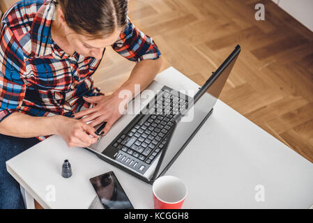 Frau Plaid Shirt sitzen auf dem Boden am Kaffeetisch und Lackieren der Nägel Stockfoto