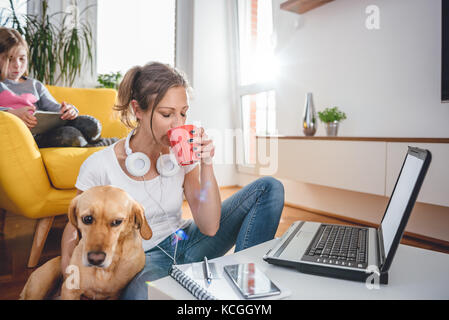 Frau mit weißem T-Shirt sitzen auf dem Boden in der Tabelle Kaffee trinken und einen Streichelzoo, einen Hund Stockfoto