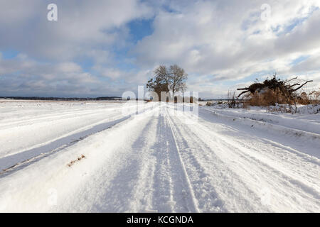 Ländliche Weg bedeckt mit Schnee im Winter. Gibt es Spuren des Autos. Vor dem Hintergrund des blauen Himmels. Stockfoto