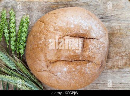 Ein Stück Roggenbrot und grüne, unreife Roggenohren liegen auf einem Holztisch. Hausgemachte Küche. Foto Nahaufnahme Stockfoto
