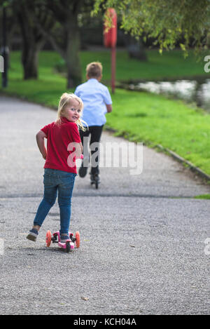 Kinder reiten Roller - zwei Kinder haben Spaß mit ihren Motorroller auf einem Weg zu reiten. Stockfoto