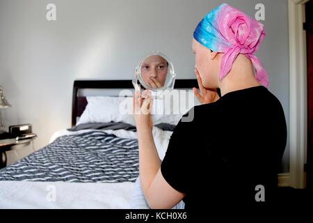 Junge Krebspatienten in einem Kopftuch sieht an der Reflexion im Spiegel schockiert Stockfoto