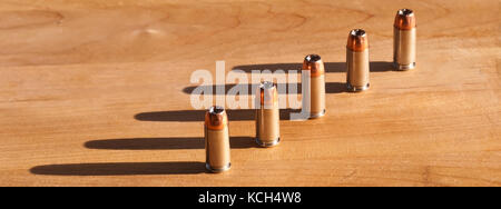 Fünf 40 Kaliber hollow point Bullets aufgereiht auf einem Holztisch mit dem Sonnenlicht Casting Shadows hinter Ihnen Stockfoto