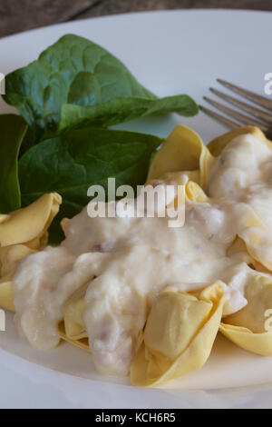 Tortellini und Spinat mit Carbonara Soße auf einer weißen Platte. Stockfoto