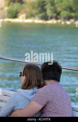 Ein junges Paar auf einem Boot mit dem Meer und den Strand im Hintergrund in Griechenland sitzen auf Korfu mit Sonnenbrille. Stockfoto