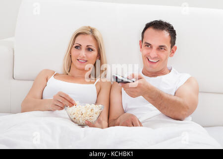 Paar am Bett mit Popcorn und Fernbedienung In der Hand vor dem Fernseher entspannen Stockfoto