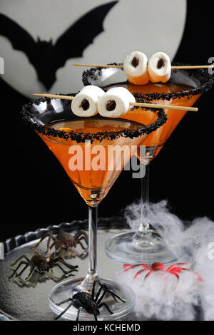 Glas von Zitrusfrüchten Martini mit schwarzen Zucker mit Marshmallow Augen auf den Tisch dekoriert zu Ehren von Halloween Stockfoto